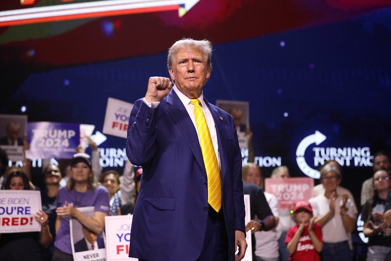 Donald Trump delivers a speech at a rally, emphasizing his campaign for the 2024 elections with supporters holding signs in the background.