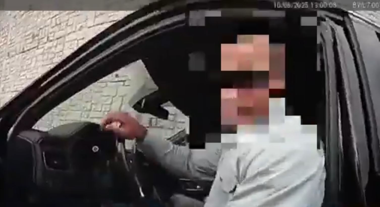A person seated in a car driver's seat, interacting with the camera, with a blurred face for privacy.