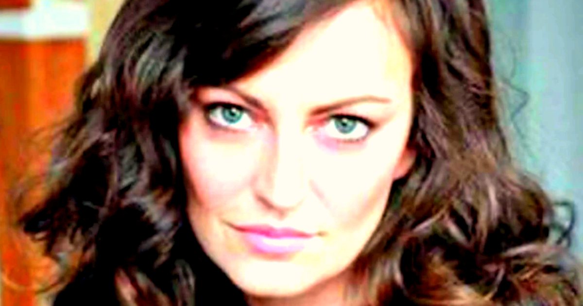 Close-up portrait of a woman with long, wavy hair and striking green eyes, showcasing a confident expression against a blurred background.