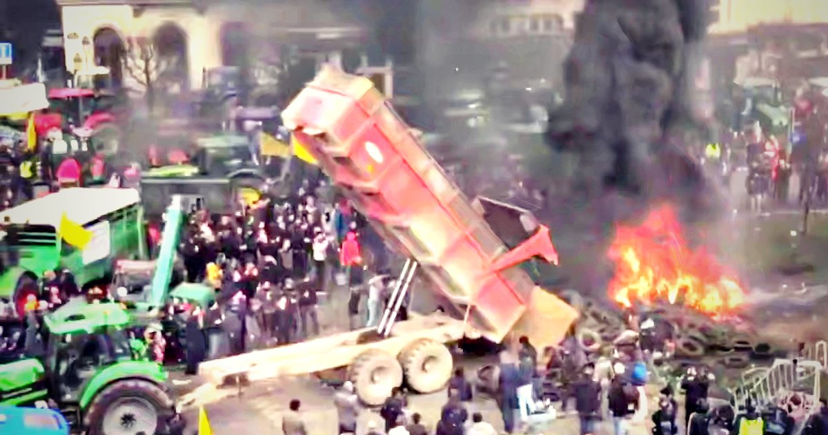 Protest scene with a tipped truck, smoke, and fire amidst a crowd of demonstrators and agricultural vehicles.