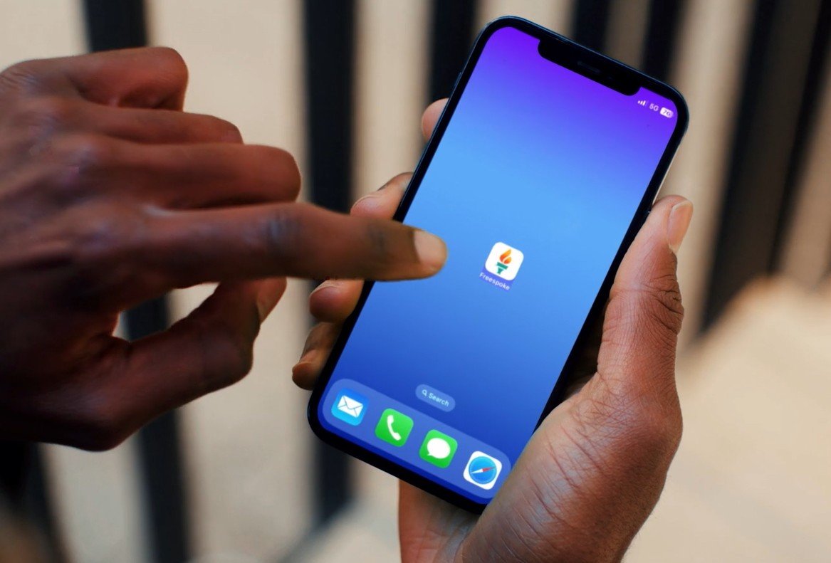 Hand holding a smartphone with a blue gradient background, featuring the FreeSpoke app icon on the screen.