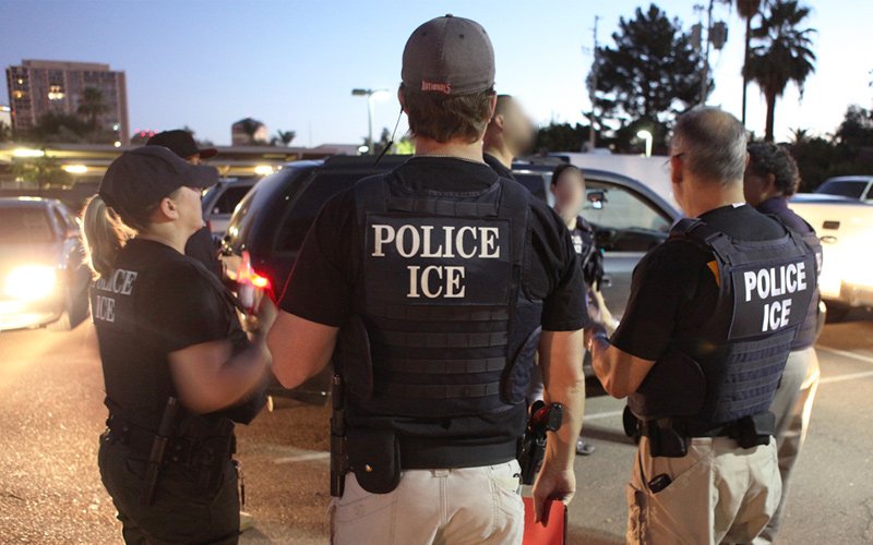 Police officers from ICE engage in a discussion during a night operation in a parking lot, emphasizing law enforcement activities.