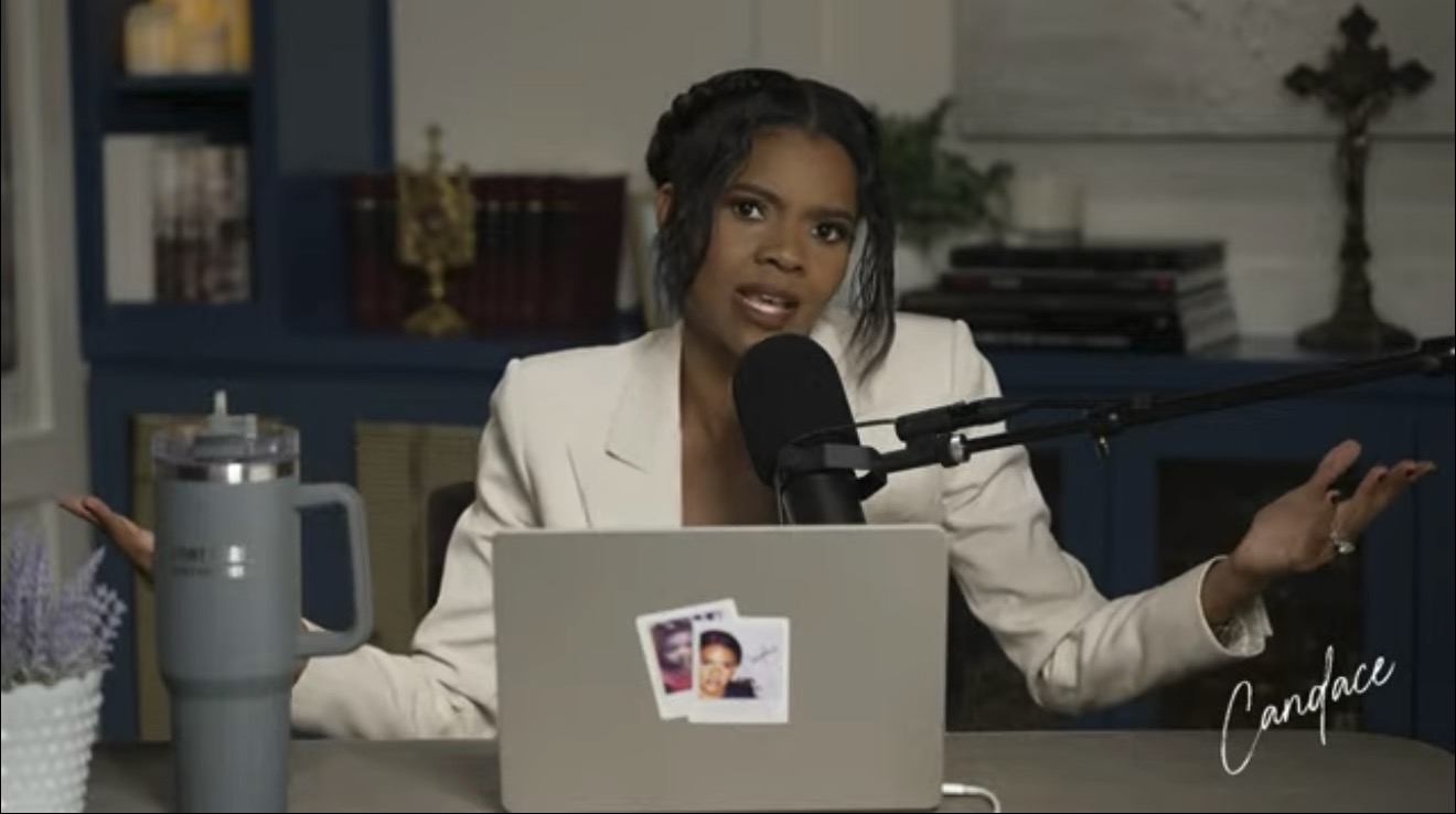 Candace Owens speaking into a microphone during a podcast episode, with a laptop and a large drink container on the table.
