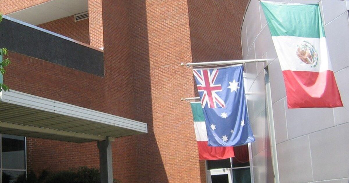 Flags of Australia, Mexico, and Italy displayed outside a modern brick building, symbolizing multiculturalism and international presence.