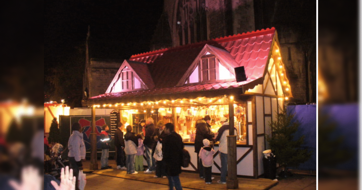 Festive market stall illuminated at night, with people shopping and enjoying seasonal treats in a charming, cozy setting.