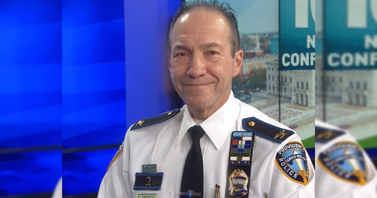Providence police chief presenting during a news conference, wearing a police uniform with various badges and insignia against a blue background.