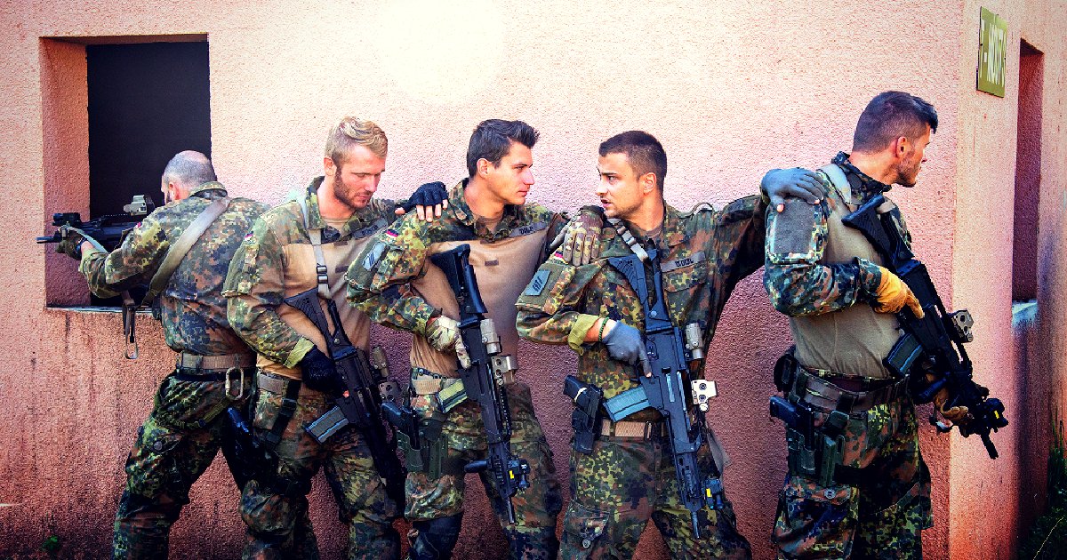 Soldiers in tactical gear prepare for a mission, showcasing teamwork and military readiness against a textured wall backdrop.