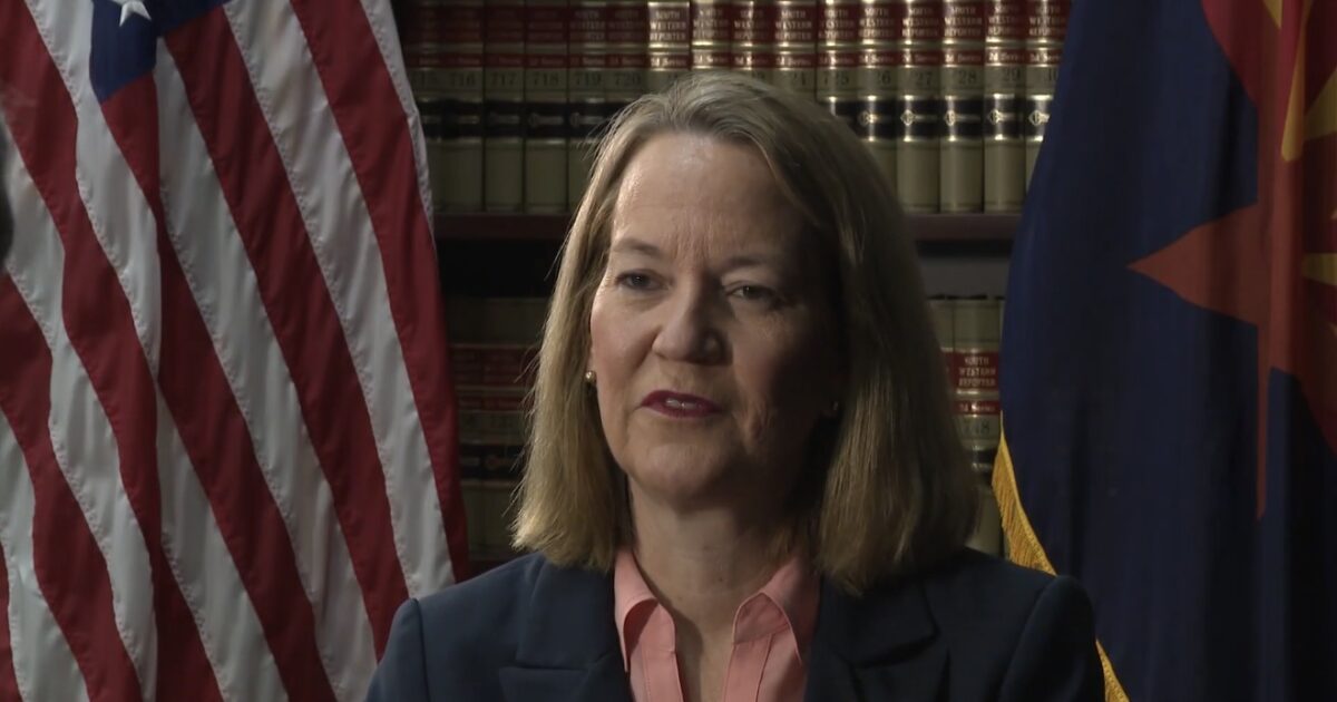 Portrait of a professional woman speaking in front of an American flag and legal books, representing authority and leadership in law or governance.