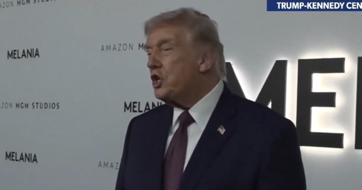 Donald Trump speaking at an event with a backdrop featuring the words "Melania" and "Amazon MGM Studios."