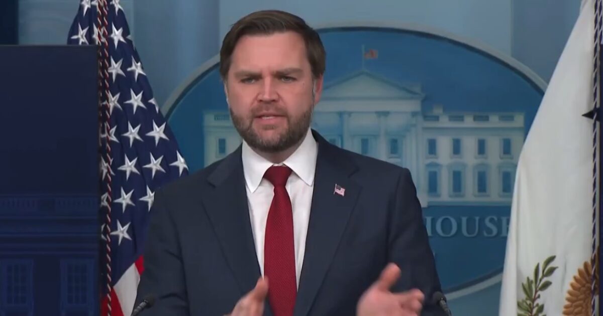 Official press briefing at the White House featuring a speaker addressing key issues, with U.S. flags in the background.