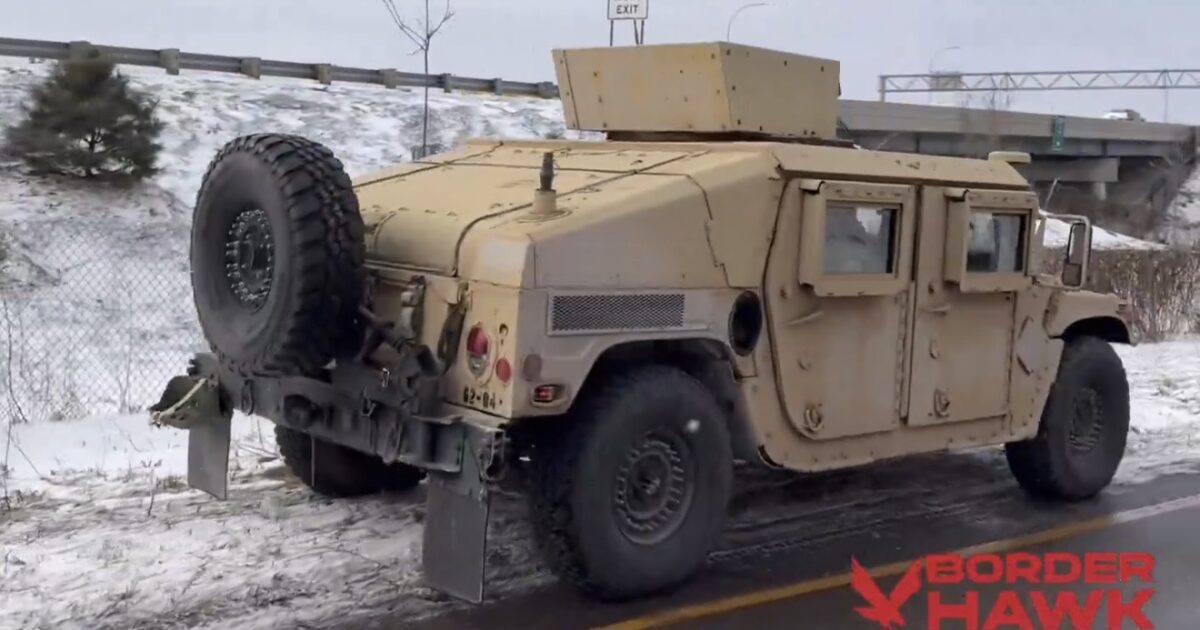 Military Humvee vehicle equipped for border patrol operations driving on a snowy road with a highway sign in the background.