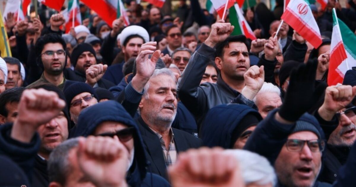 Crowd of protesters waving Iranian flags and raising fists during a demonstration, showcasing solidarity and political activism in Iran.
