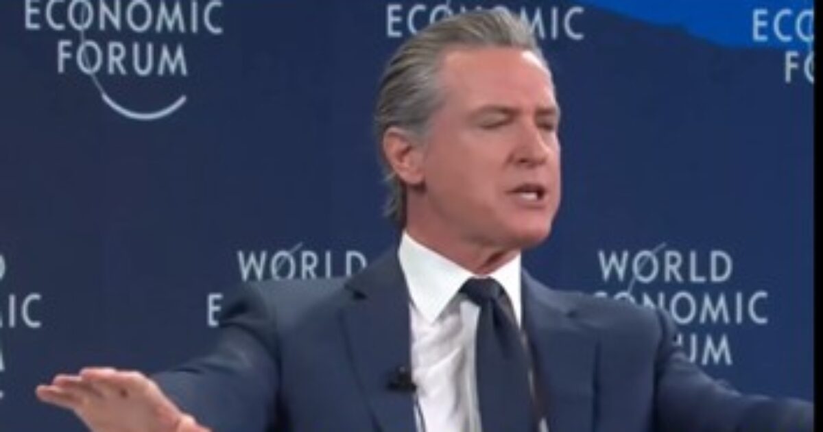 Gavin Newsom speaking at the World Economic Forum, gesturing while discussing key issues in front of a branded backdrop.