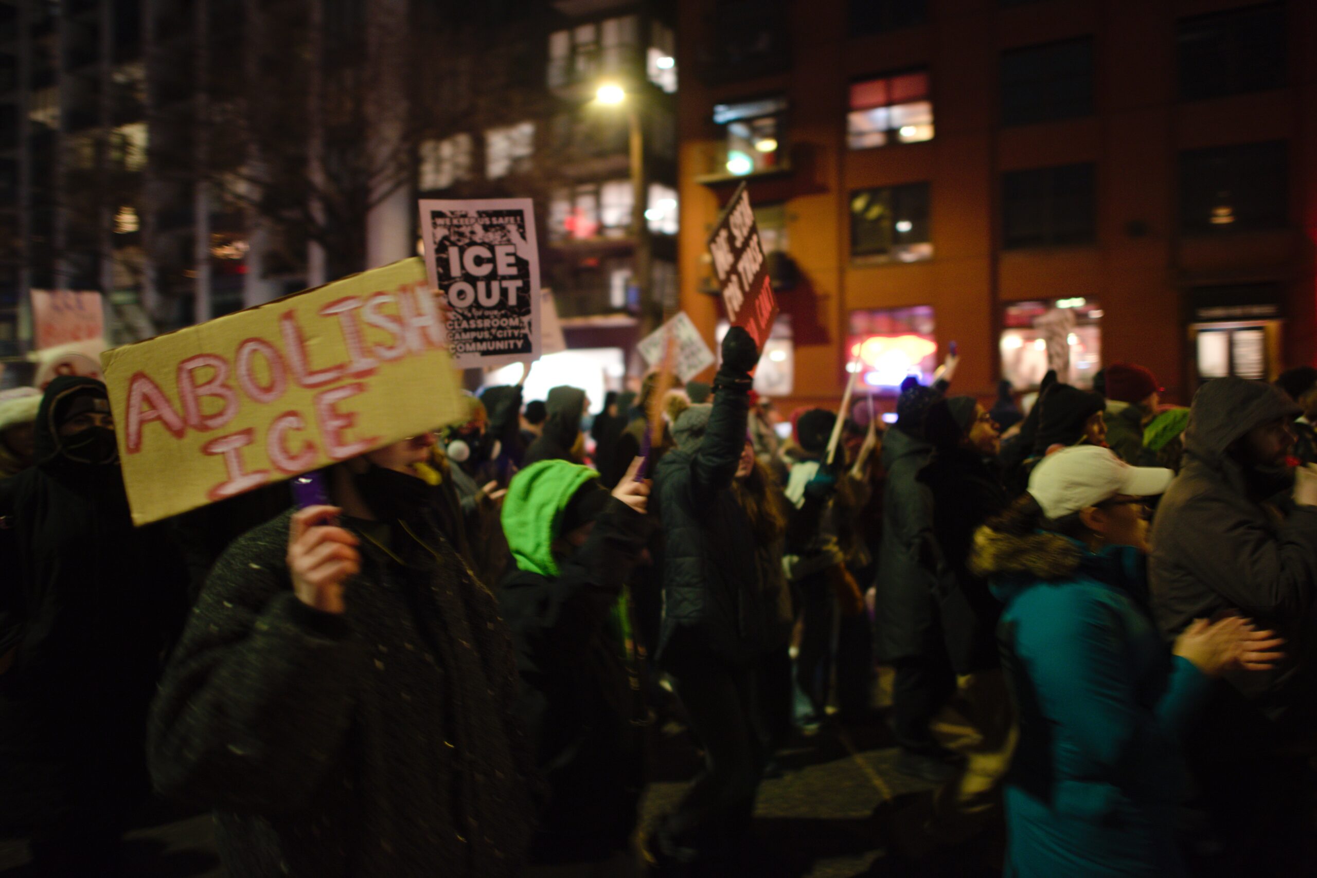 Demonstrators hold signs advocating to abolish ICE during a nighttime protest in an urban setting.