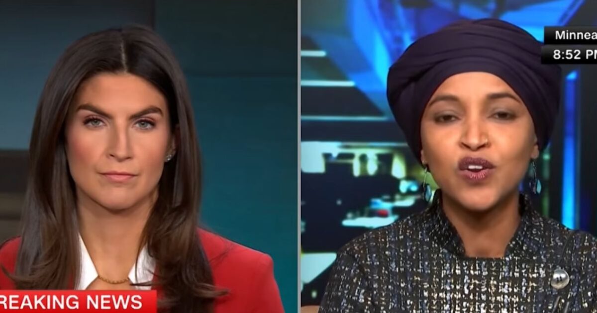 News anchors discussing breaking news, featuring a woman in a red blazer and another in a dark outfit and headscarf, with a digital backdrop.