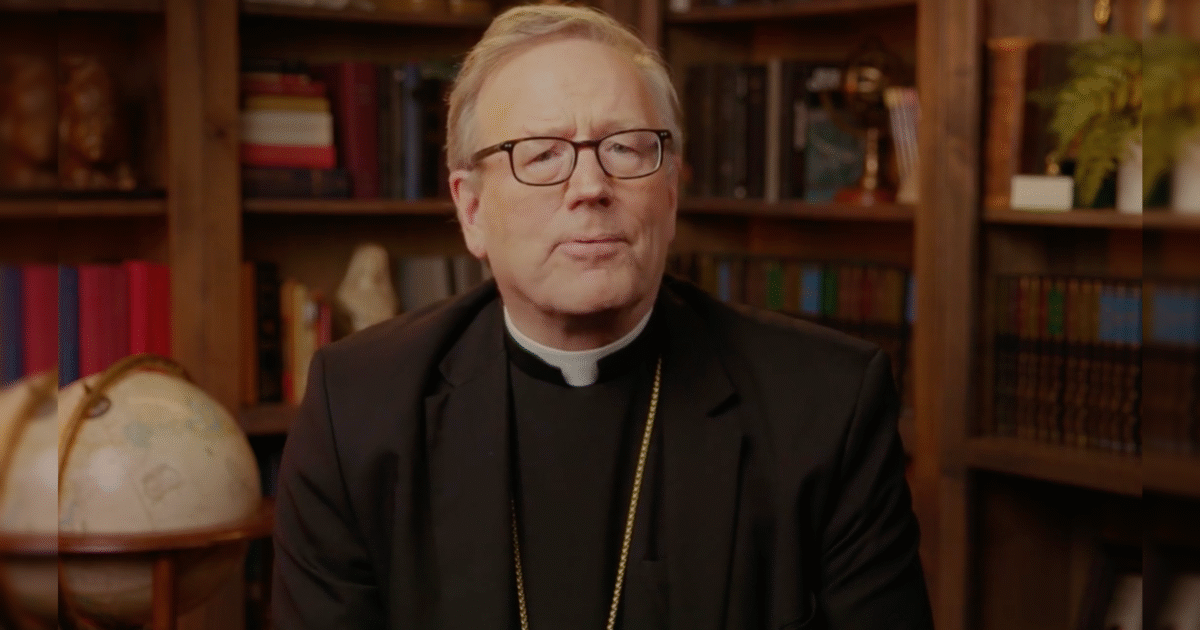 Clergyman in a black suit and glasses speaking in front of a bookshelf and globe, conveying a message with a thoughtful expression.