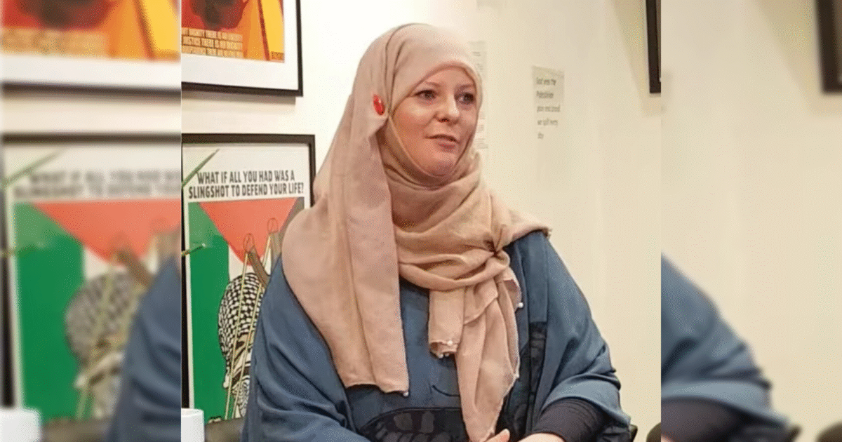 Woman wearing a beige hijab and blue top speaking at an event, with colorful artwork featuring social justice themes in the background.