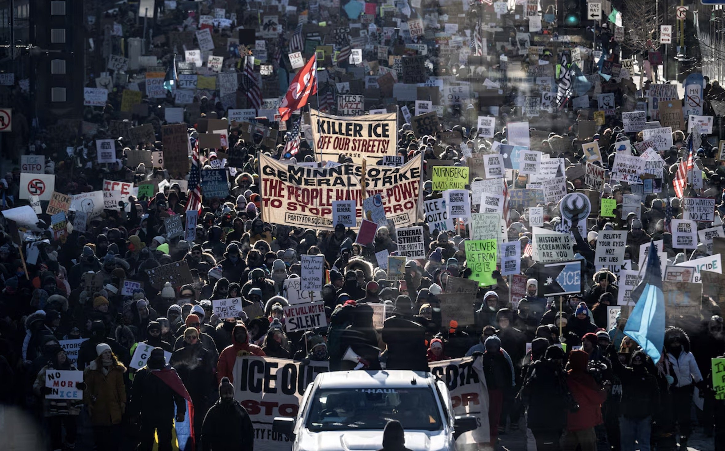 Crowd of protesters holding signs at a rally against ICE, advocating for immigrant rights and social justice in a city setting.