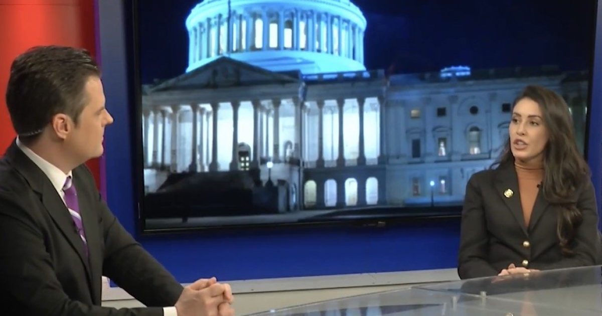 Two news anchors discuss current events on set, with the illuminated U.S. Capitol building visible in the background at night.