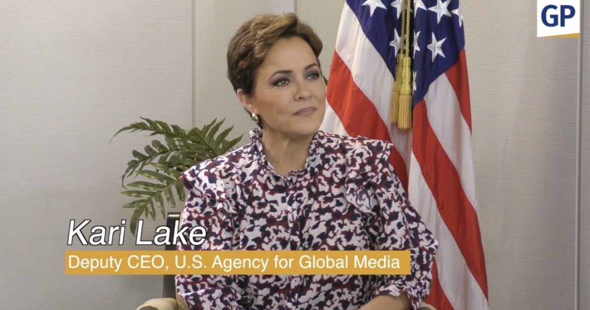 Kari Lake, Deputy CEO of the U.S. Agency for Global Media, seated with U.S. flag backdrop, discussing media and communication strategies.