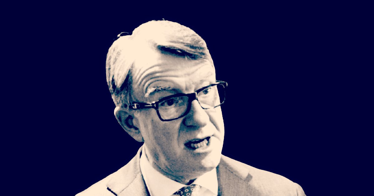 Business professional with glasses speaking passionately against a dark background, showcasing engagement and confidence in a corporate setting.