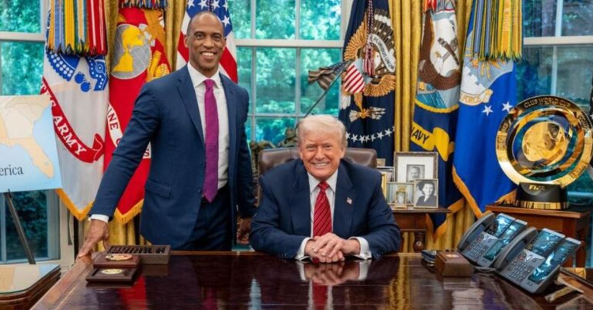 Former President Donald Trump and an associate pose in the Oval Office, surrounded by flags and official decor, with a map and awards visible on the desk.