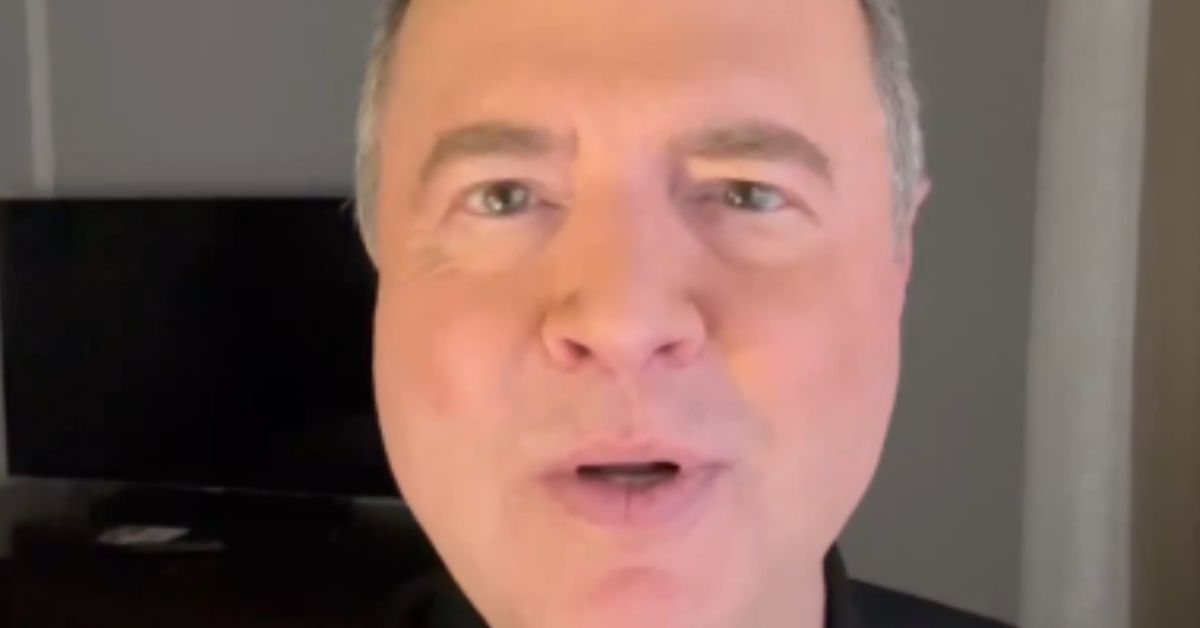 Close-up of a man speaking directly to the camera in a well-lit room with a television in the background.