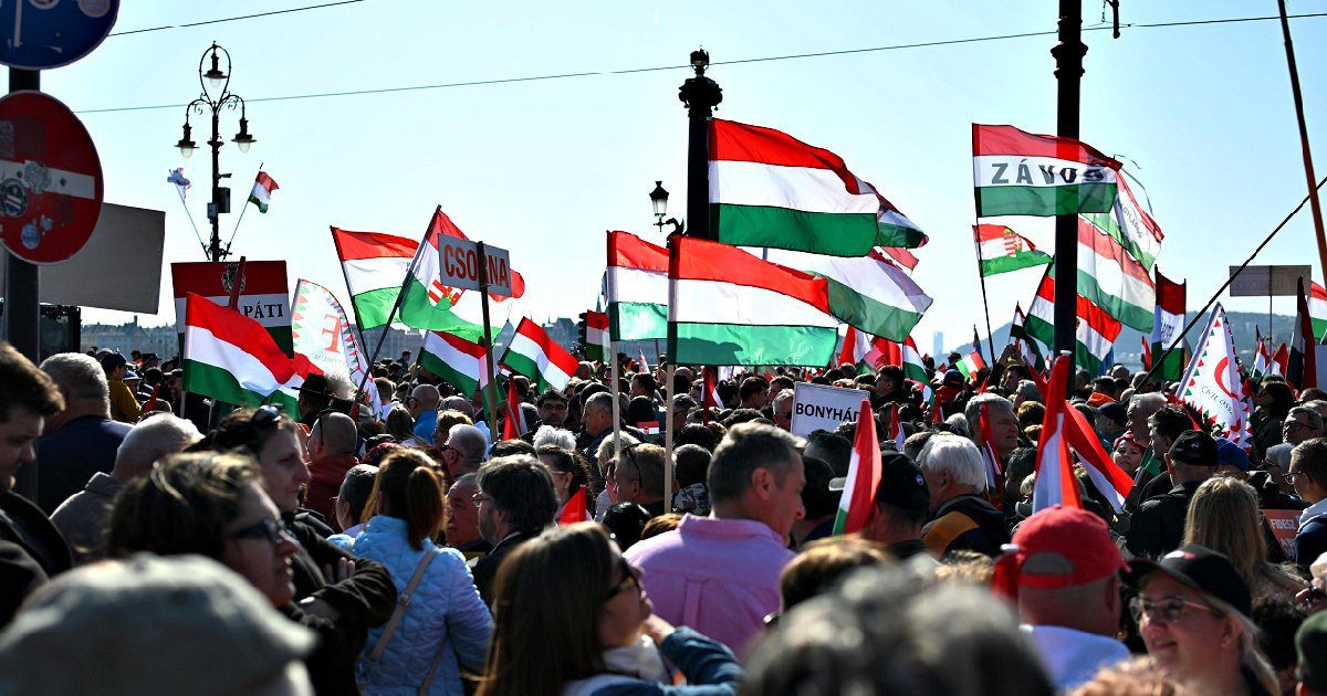 Crowd of protesters waving Hungarian flags during a demonstration in a city square under clear blue skies.
