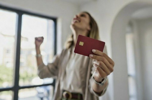 Woman celebrating with a red credit card in hand, expressing joy and success in a bright indoor setting.