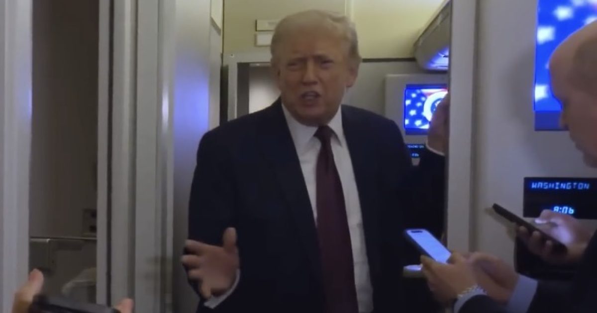Donald Trump speaking to reporters aboard an airplane, with journalists holding smartphones and recording the interaction in a narrow aisle.