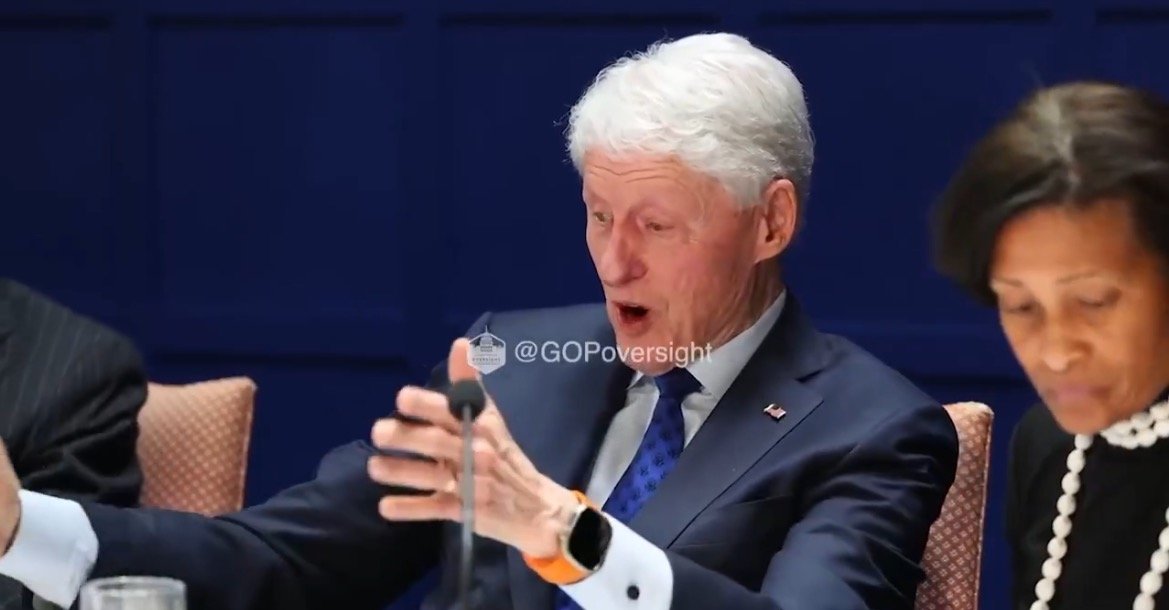 Bill Clinton engaged in a discussion, expressing enthusiasm with hand gestures, while seated at a panel alongside two other individuals.