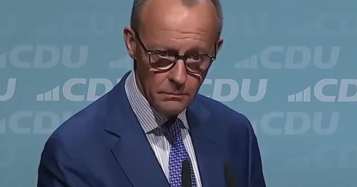 Politician in a blue suit and glasses stands at a podium during a CDU press conference, presenting a serious expression against a light blue background.