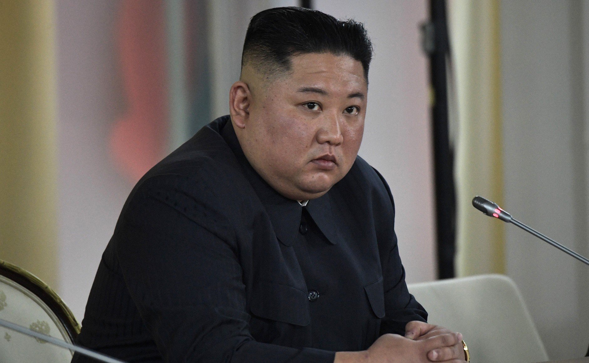 North Korean leader Kim Jong-un seated at a conference table, looking serious during a meeting with officials.
