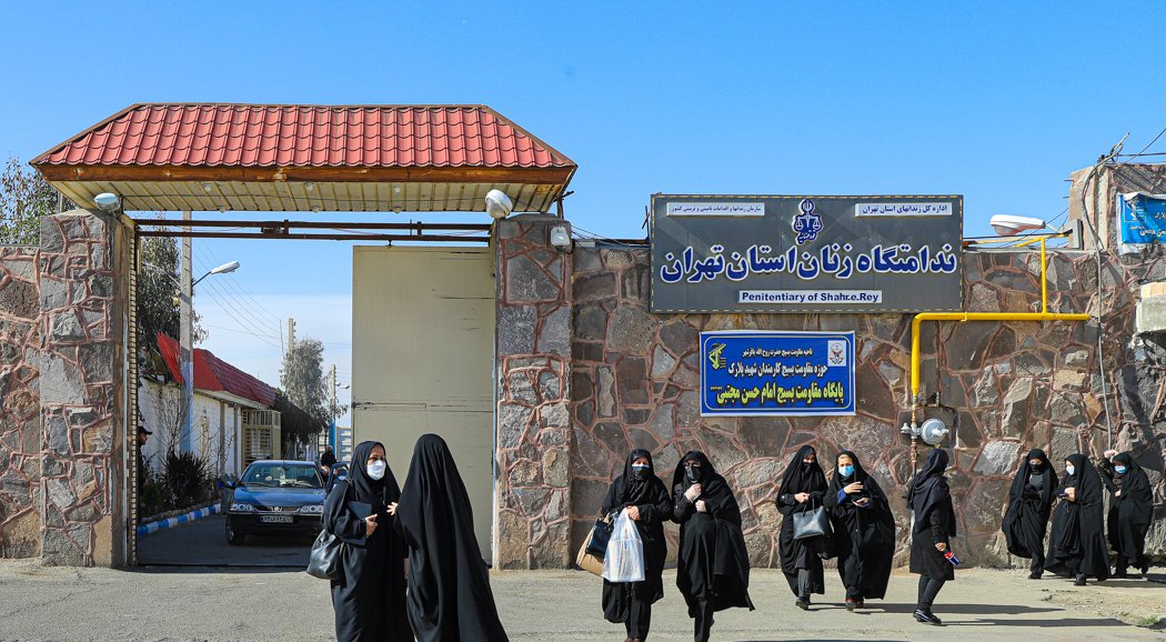 Women in black chadors exit the Shahre-Rey Penitentiary in Tehran, highlighting the cultural attire and the facility's architecture.