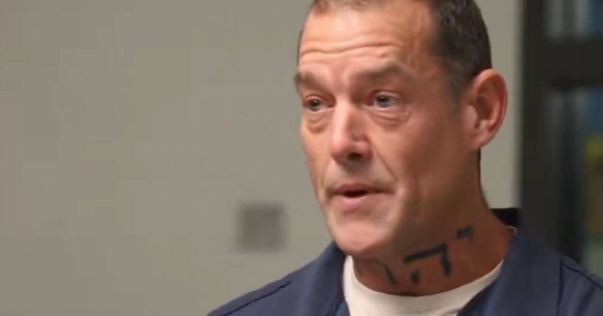 Man with facial tattoos speaking in a casual setting, wearing a blue shirt, with a neutral background.
