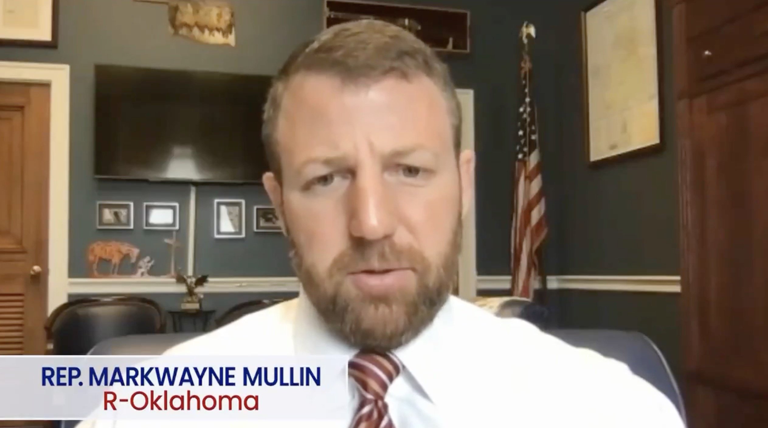 Representative Markwayne Mullin from Oklahoma speaking during a virtual meeting, with an American flag and framed pictures visible in the background.
