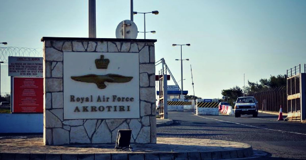 Royal Air Force Akrotiri entrance sign with a vehicle approaching, set against a clear sky and security barriers.