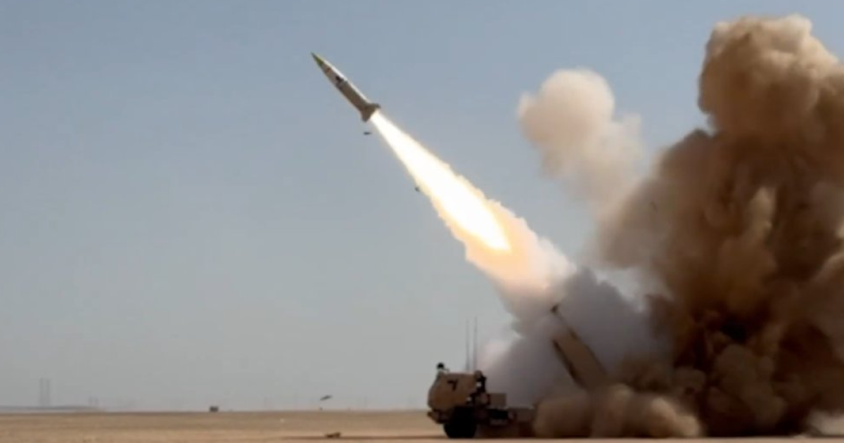 Missile launch from a mobile artillery platform, surrounded by smoke and dust in a desert landscape.