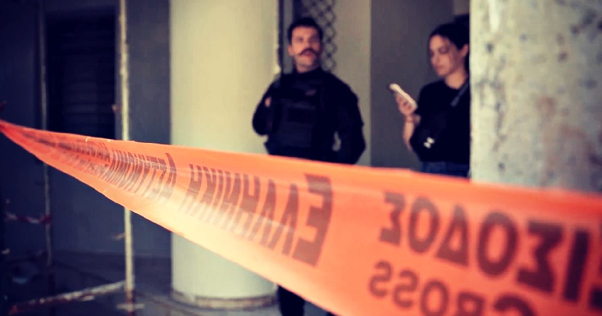 Police officers stand near orange caution tape in a partially constructed building, indicating a restricted area during an investigation.