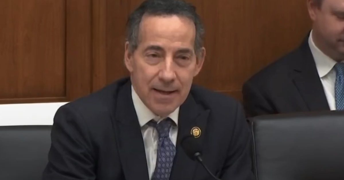 Congressman Raskin speaking during a congressional hearing, seated at a table with water bottles and colleagues in the background.