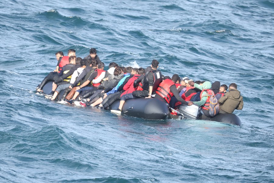A crowded inflatable boat carrying migrants navigates rough ocean waters, highlighting the challenges faced during perilous sea crossings.