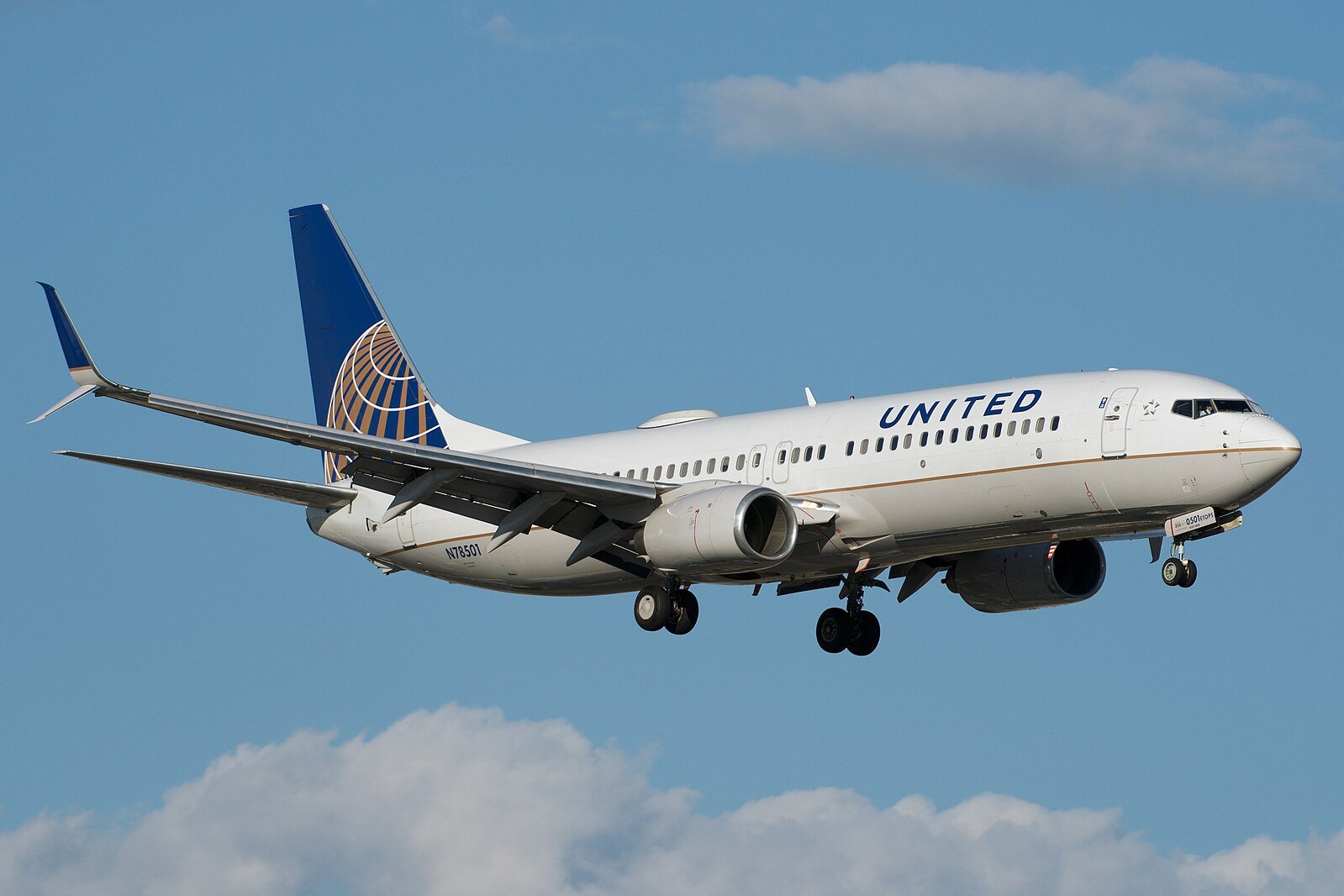 United Airlines Boeing 737 approaching for landing against a clear blue sky with scattered clouds.