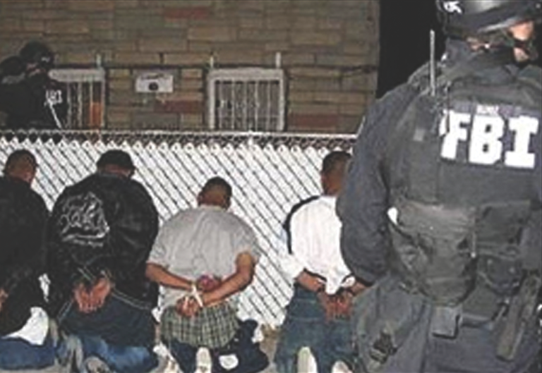 FBI agents apprehend suspects during a nighttime operation, with individuals handcuffed and seated against a fence.