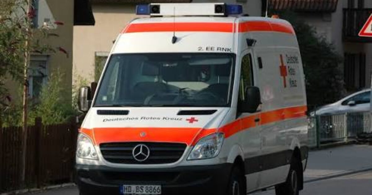 Emergency ambulance from the German Red Cross, featuring distinctive red cross markings, driving on a residential street.