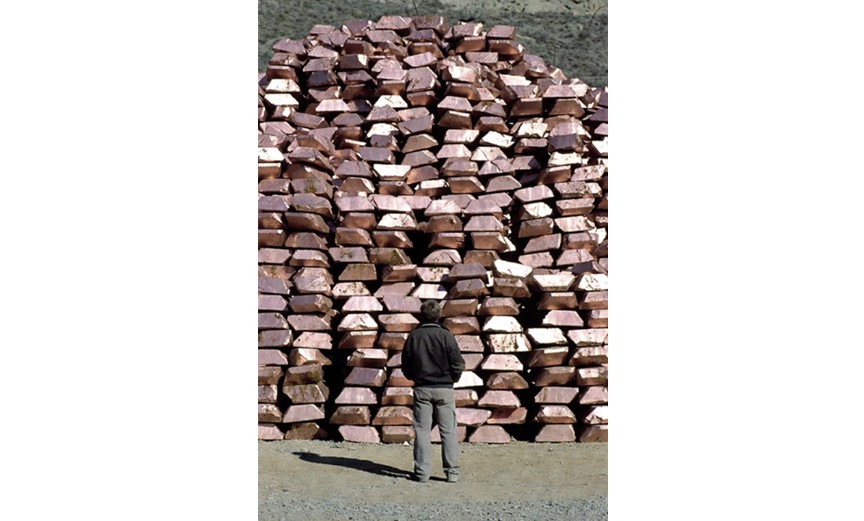 Man observing a large pile of copper ingots in an industrial setting, highlighting the scale of metal production and storage.