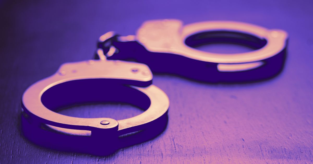 Close-up of metallic handcuffs resting on a dark surface with a purple tint, symbolizing law enforcement and criminal justice themes.