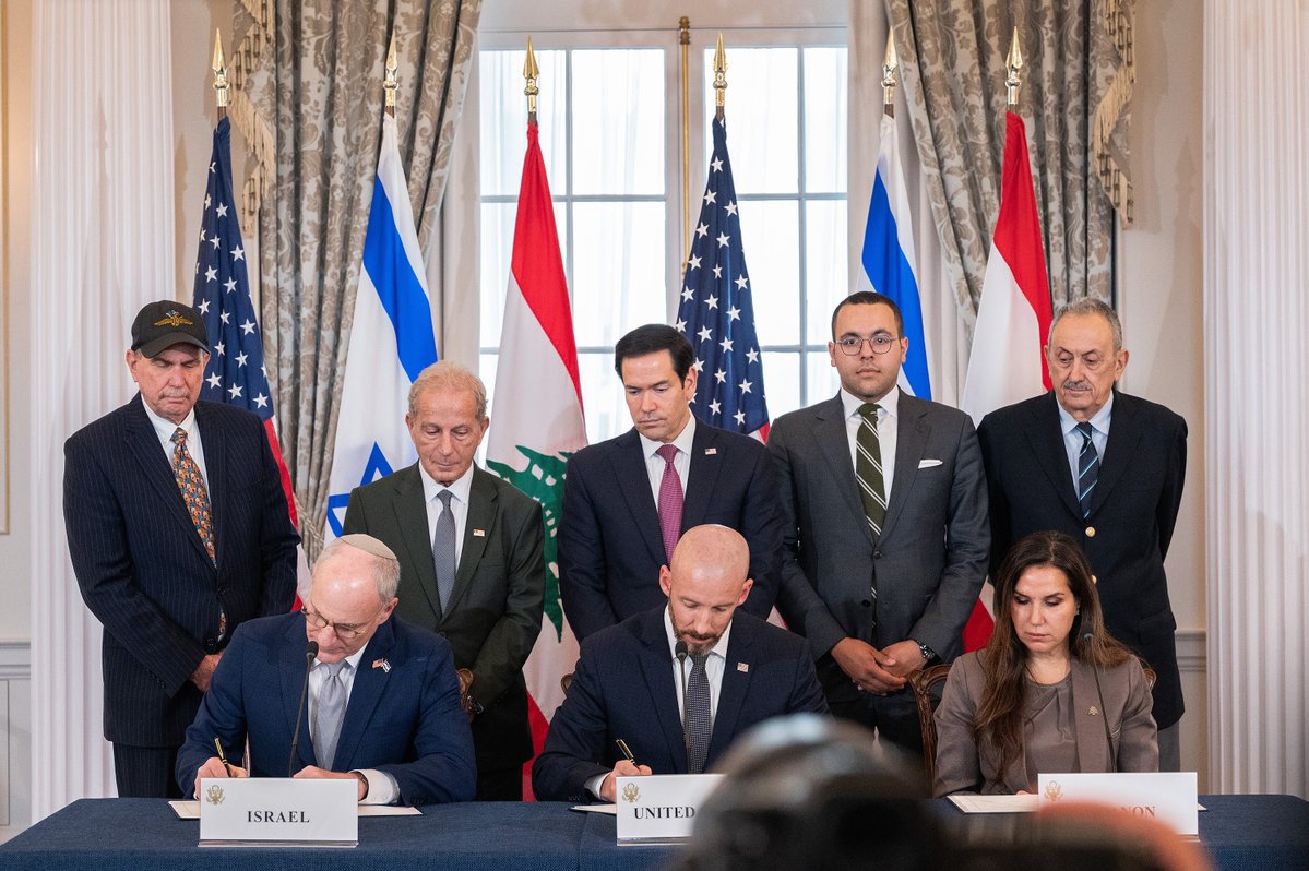 Leaders from Israel, the United States, and Lebanon sign a historic agreement, surrounded by representatives from various nations, in a formal setting with flags displayed.