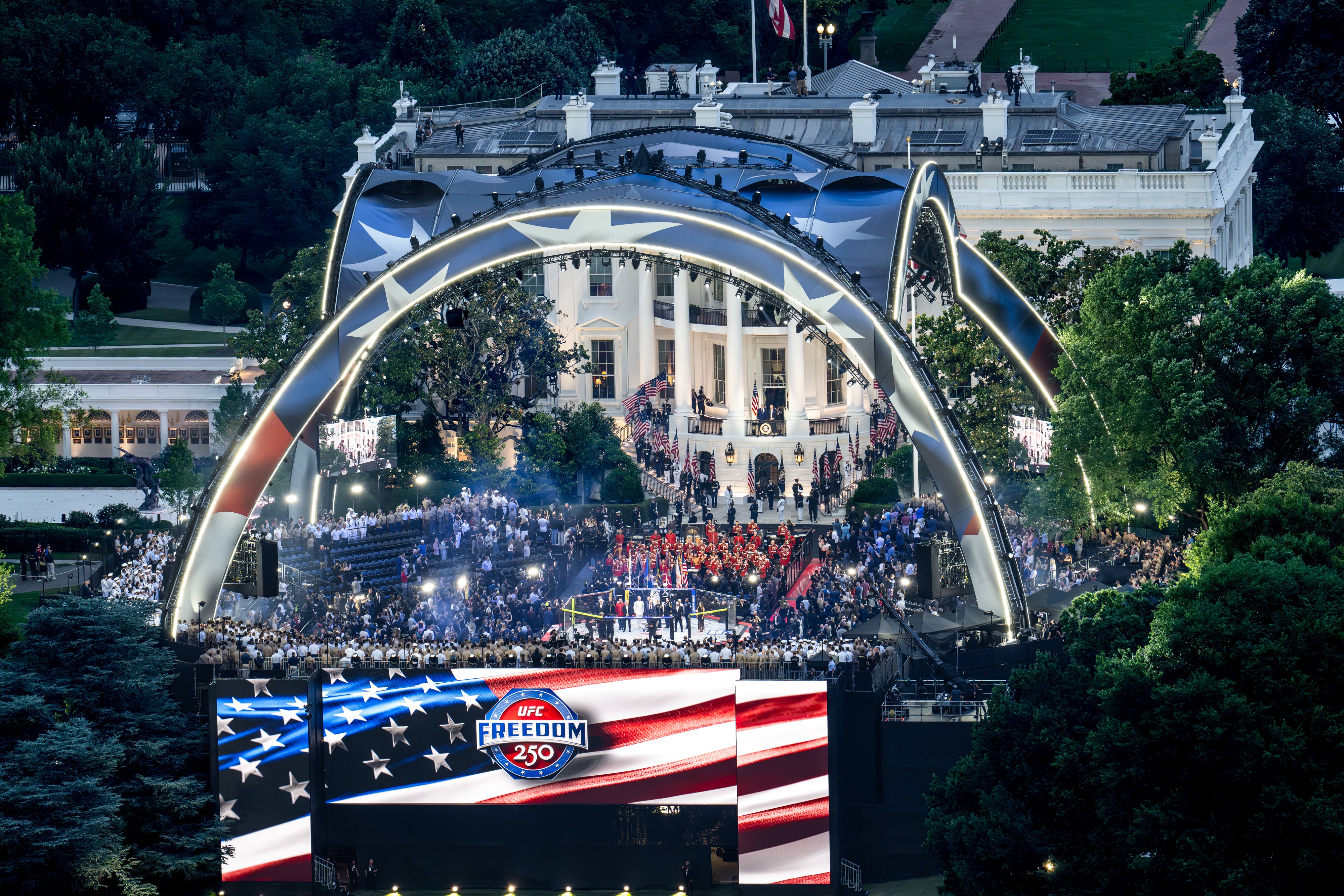 Aerial view of a large crowd gathered for the UFC Freedom 250 event outside the White House, featuring a stage and American flags.