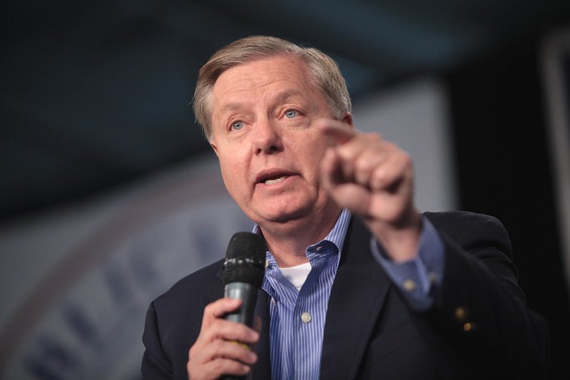 Lindsey Graham speaking passionately into a microphone at a political event, gesturing with his hand to emphasize his points.