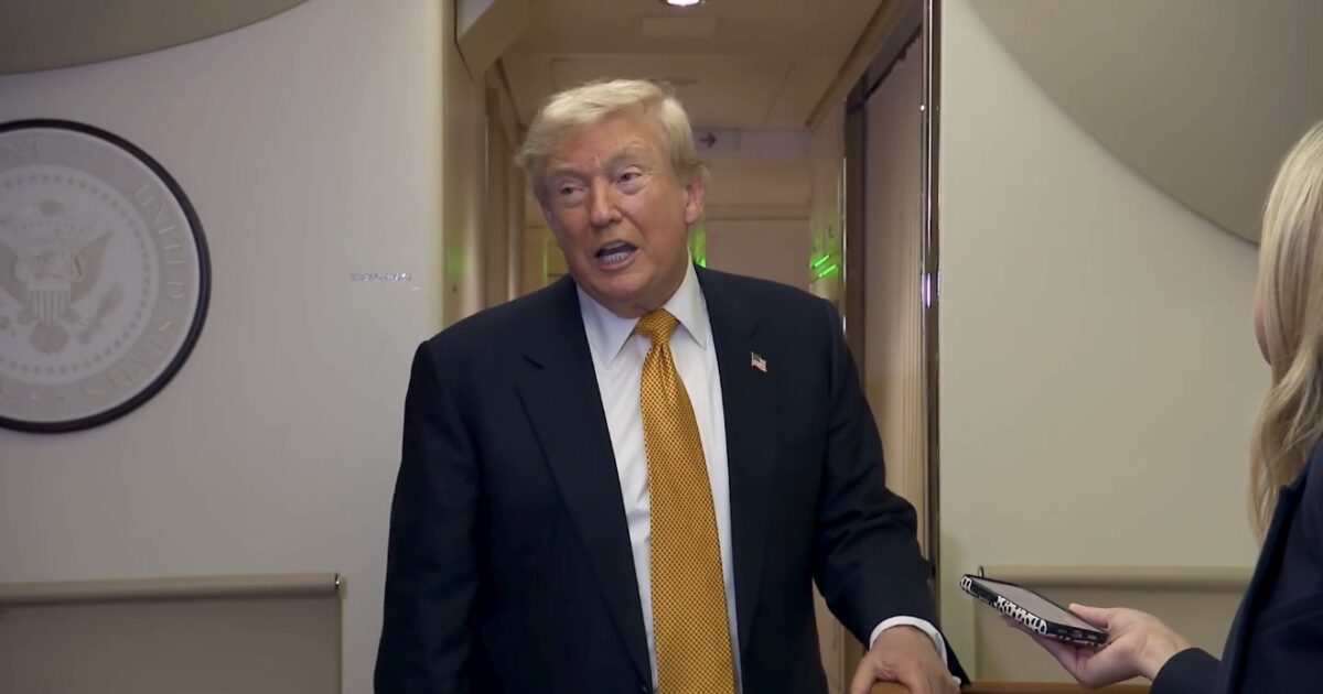 Donald Trump speaks to a reporter in a hallway, showcasing the Presidential Seal in the background, highlighting a moment during his presidency.
